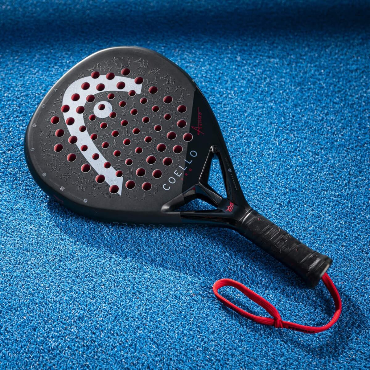 De zwarte padel racket Coello Pro 2025 met wit Head logo en het woord Coello onderaan, liggend op een blauw padel veld.