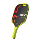 Schuin vooraanzicht van een zwarte pickleball racket met gele rand en geel handvat. Op het slagoppervlak staan rode/oranje letters.